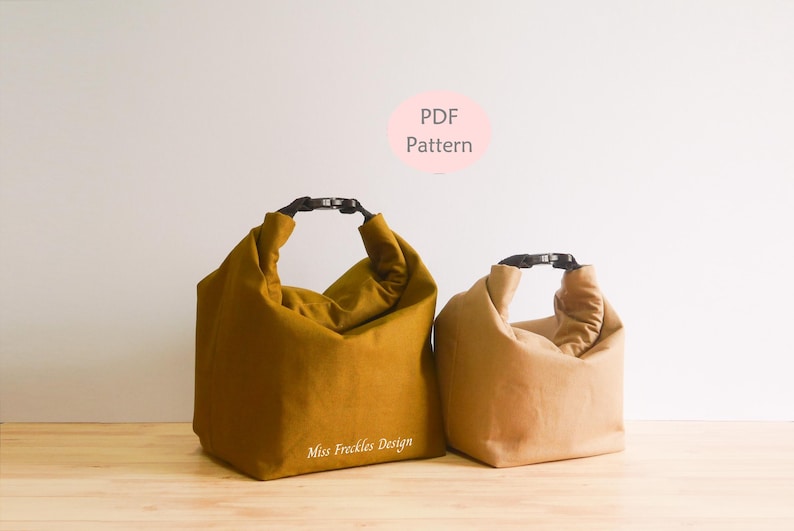 Pode incluir: Duas bolsas com fecho de enrolar e fivelas de pl&aacute;stico preto. A bolsa maior &eacute; amarelo-mostarda com o texto Miss Freckles Design, e a bolsa menor &eacute; bege. Um c&iacute;rculo rosa acima cont&eacute;m o texto PDF Pattern.