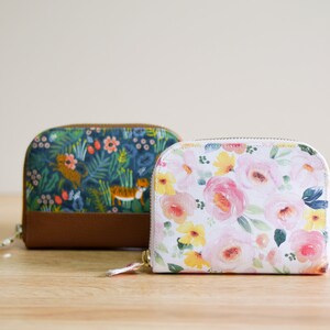 May include: Two small zippered wallets with floral patterns. One wallet has a blue and green floral pattern with tigers, the other has a white background with pink and yellow flowers.
