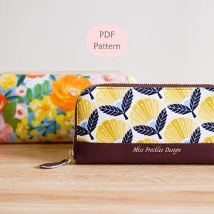 Könnte beinhalten: Zwei rechteckige Reißverschlusstaschen. Die vordere Tasche zeigt ein gelb-dunkelblaues Blumenmuster mit einem einfarbigen dunkelbraunen Boden und dem Text Miss Freckles Design. Die hintere Tasche hat einen bunten Blumendruck.