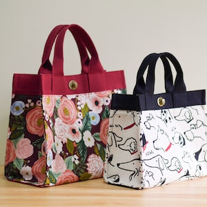 Pu&ograve; includere: Due borse a mano, una con stampa floreale e l'altra con stampa di cani in bianco e nero. La borsa floreale &egrave; color borgogna con un motivo floreale in tonalit&agrave; rosa, rosso e blu. La borsa per cani &egrave; bianca con illustrazioni di cani in bianco e nero.