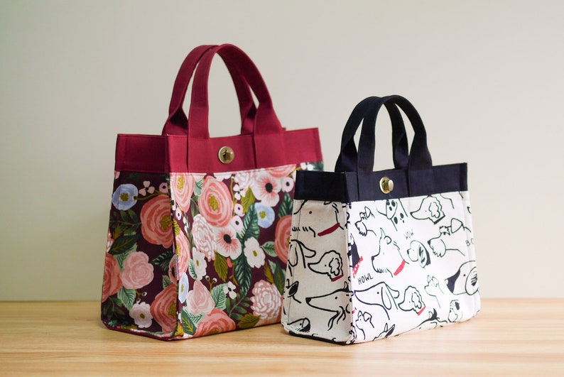 Pu&ograve; includere: Due borse a mano, una con stampa floreale e l'altra con stampa di cani in bianco e nero. La borsa floreale &egrave; color borgogna con un motivo floreale in tonalit&agrave; rosa, rosso e blu. La borsa per cani &egrave; bianca con illustrazioni di cani in bianco e nero.