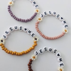 May include: Four beaded bracelets with the words "Jesus Loves Me" spelled out on each bracelet. The bracelets are in different colors: purple, pink, yellow, and brown.