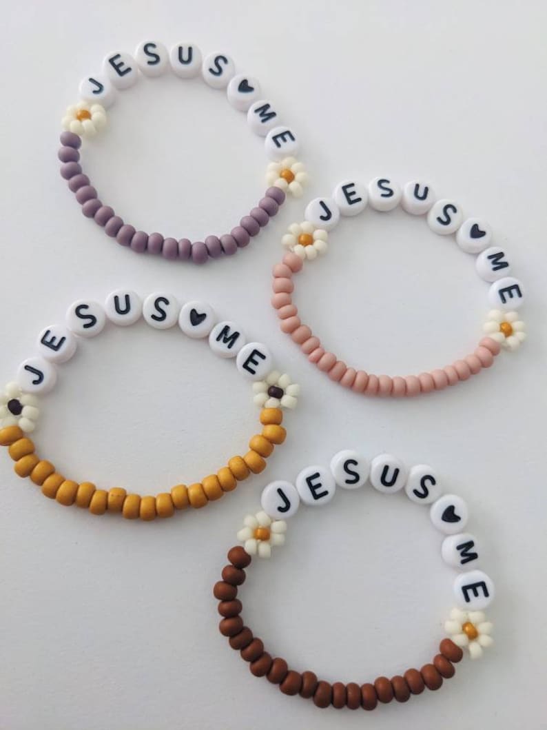 May include: Four beaded bracelets with the words "Jesus Loves Me" spelled out on each bracelet. The bracelets are in different colors: purple, pink, yellow, and brown.