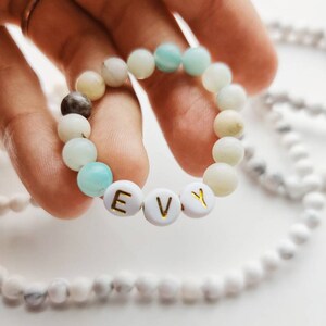 May include: A light blue and white beaded bracelet with the name "EVY" spelled out in gold letters on white beads.