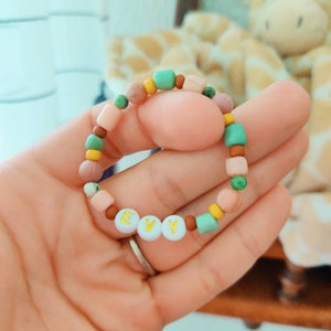 May include: A colourful beaded bracelet with the name "EVY" spelled out in white beads with gold lettering.
