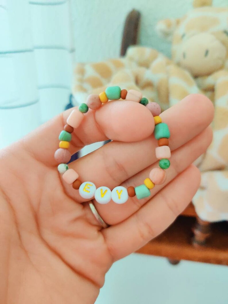 May include: A colourful beaded bracelet with the name "EVY" spelled out in white beads with gold lettering.