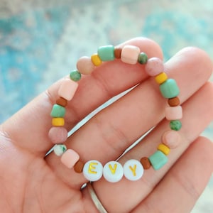 May include: A pink, brown and green beaded bracelet with the name "EVY" spelled out in gold letters on white beads.