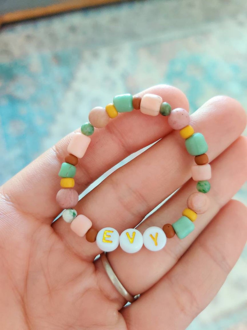 May include: A pink, brown and green beaded bracelet with the name "EVY" spelled out in gold letters on white beads.