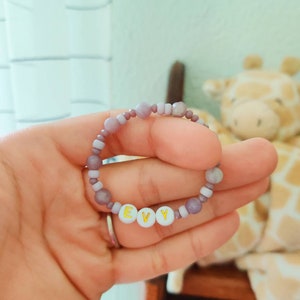 May include: A purple and white beaded bracelet with the name "EVY" spelled out in gold letters on white beads.