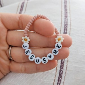May include: A pink beaded bracelet with white daisy beads and black letter beads spelling "JESUS LOVES ME".