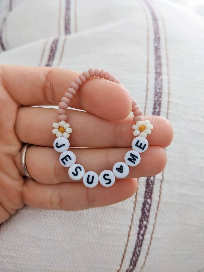 May include: A pink beaded bracelet with white daisy beads and black letter beads spelling "JESUS LOVES ME".