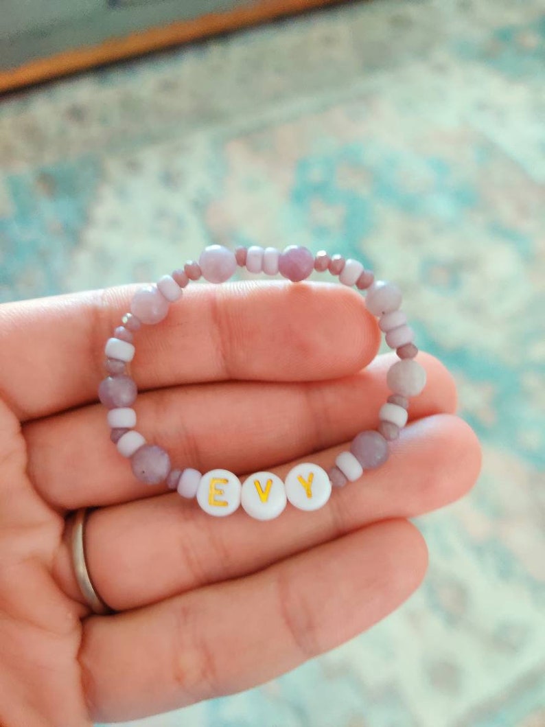 May include: A purple and white beaded bracelet with the name "EVY" spelled out in gold letters on white beads.