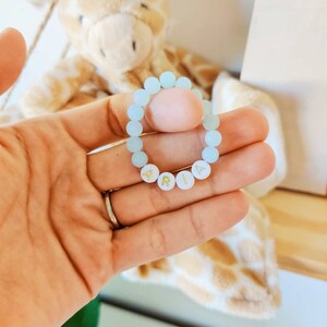 May include: A light blue beaded bracelet with the name "ARIA" spelled out in gold letters.