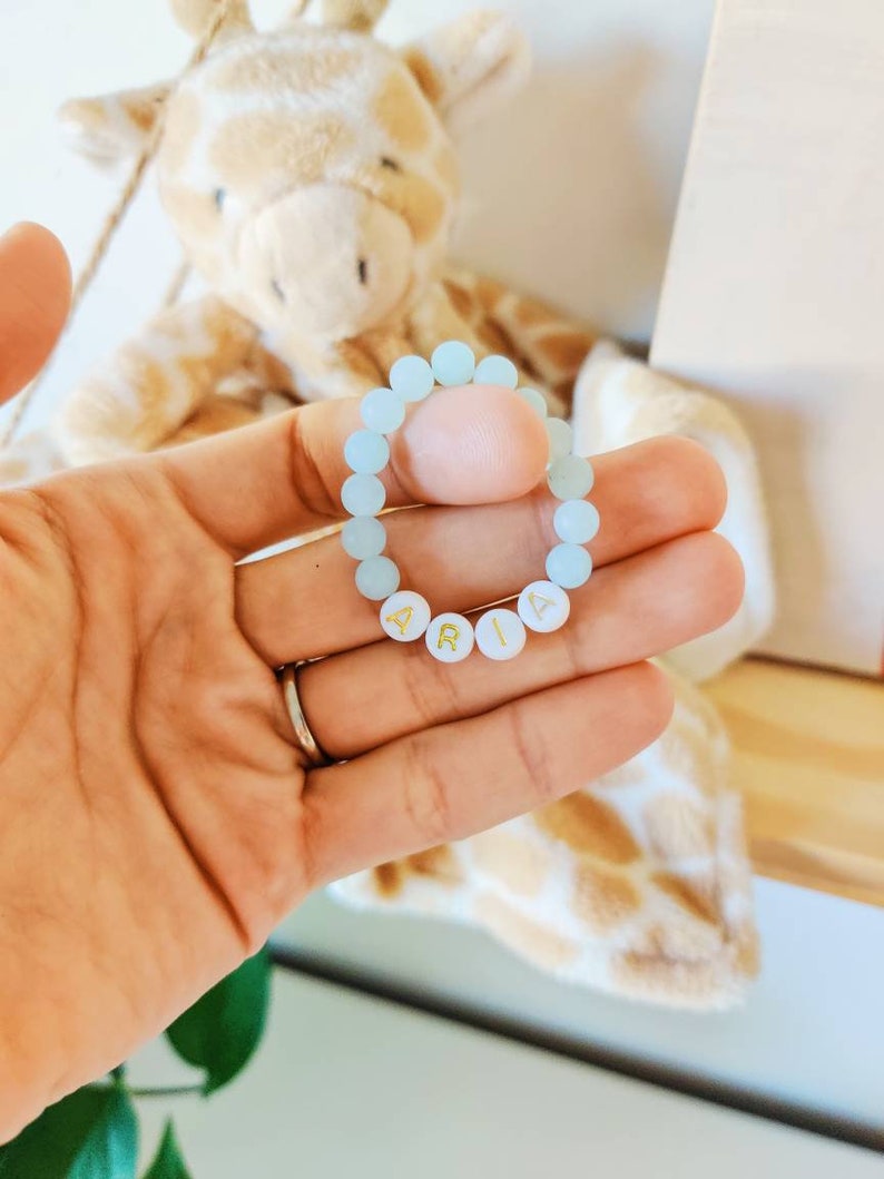 May include: A light blue beaded bracelet with the name "ARIA" spelled out in gold letters.