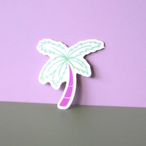 May include: A palm tree sticker with a white outline, light green fronds, and a pink trunk. The sticker is set against a two-tone background of lavender and gray.