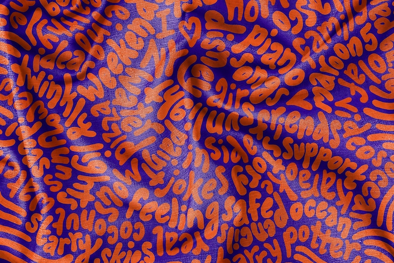 May include: A blue fabric background with orange text printed on it. The text is in a variety of fonts and sizes and includes words like "ideas", "weekend", "friends", "safe", "jokes", "feeling", "ocean", and "love".