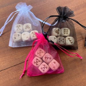 May include: Three small organza bags, white, black, and hot pink, each containing six wooden dice. The dice are light-colored with dark brown etched designs of a mouse head and Mickey Mouse gloves. The bags are tied with matching satin ribbons.