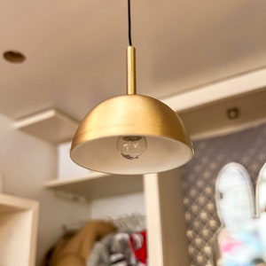 May include: A gold pendant light fixture with a white shade and a light bulb. The light is hanging from a black cord.