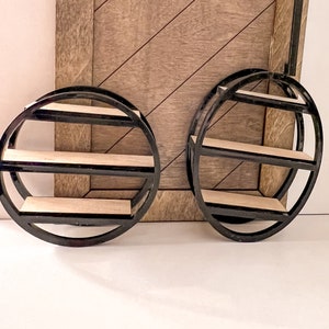 May include: Two black metal round shelves with three tiers each. The shelves are mounted on a wood wall.