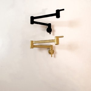 May include: Two metal faucet arms, one black and one gold, are shown against a white background. The arms are in a folded position.