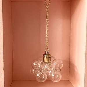 May include: A gold chain hangs from the ceiling of a pink room, suspending a clear glass bubble pendant light.