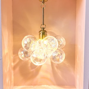 May include: A gold-toned pendant light fixture with a cluster of clear glass globes. The light fixture is hanging from a ceiling in a white square recess.