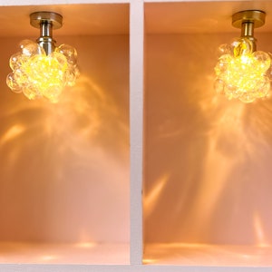 May include: Two gold ceiling light fixtures with clear glass shades that resemble clusters of bubbles. The lights are mounted in a white, square, recessed ceiling.