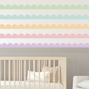 May include: A nursery room with a cot and a chair. The wall is decorated with a scalloped border in pastel colours, including green, blue, orange, pink, and purple.