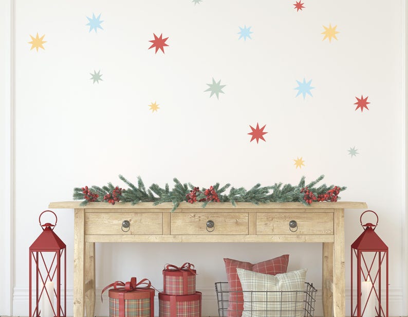 May include: A festive scene with a wooden console table adorned with a garland of greenery and red berries. Red lanterns flank the table, and gifts are stacked below. Colorful star decals decorate the white wall, creating a cheerful holiday ambiance.