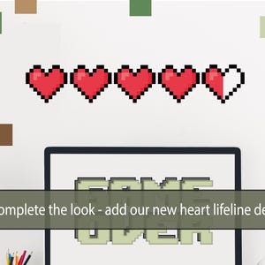 Pu&ograve; includere: Un muro bianco con una fila di cuori pixelati rossi, un monitor di computer con la scritta "GAME OVER" sullo schermo e il testo "Completa il look - aggiungi i nostri nuovi adesivi di linea di vita a forma di cuore".
