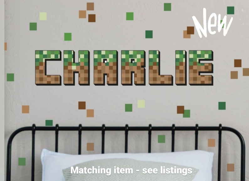 Pu&ograve; includere: Un adesivo da parete a tema Minecraft con il nome "CHARLIE" in lettere di blocchi pixelate. Le lettere sono marroni con blocchi di erba verde in cima. Lo sfondo &egrave; un muro grigio chiaro con blocchi pixelati verdi e marroni sparsi.