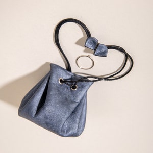 May include: A small, gray drawstring pouch with a black cord and a silver ring. The pouch is made of a textured material and has a drawstring closure.