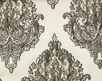 May include: A white fabric with a repeating pattern of gold damask designs. The fabric has a subtle sheen and a luxurious feel.