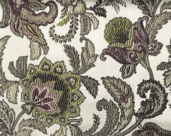 May include: A white fabric with a floral pattern in shades of green, brown, and purple. The fabric has a textured, raised design.