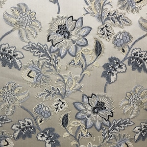 May include: A beige fabric with a floral pattern in shades of blue and grey. The flowers are stylised and have a vintage look.