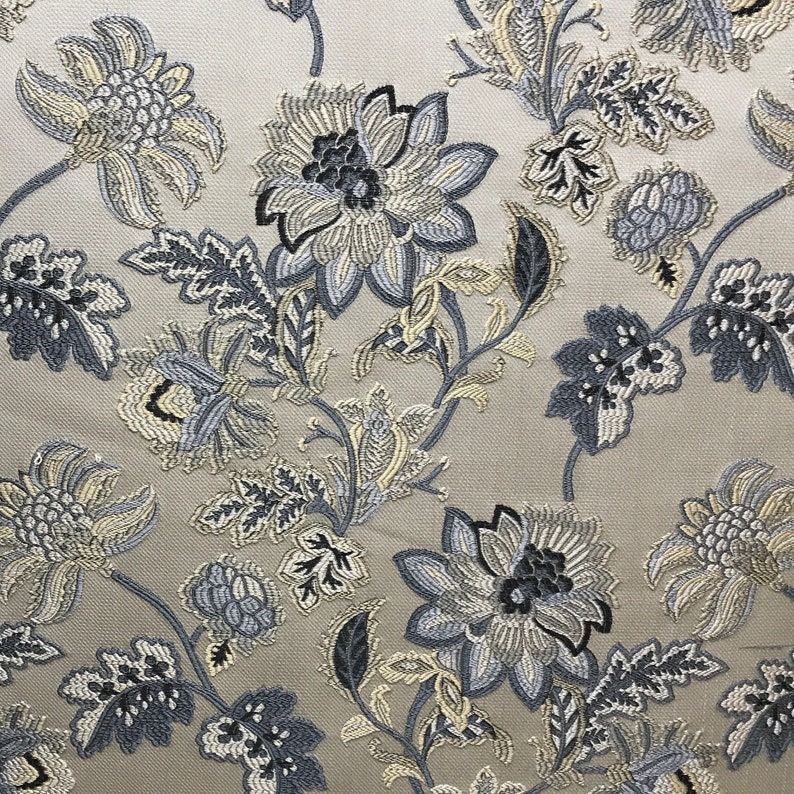 May include: A beige fabric with a floral pattern in shades of blue and gray. The flowers are stylized and have a vintage look.
