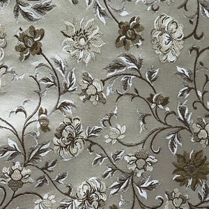 Puede incluir: Tela beige con un patrón floral. Las flores son blancas y marrones con una textura en relieve.