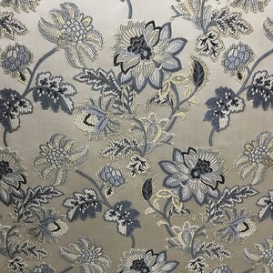 May include: A beige fabric with a repeating pattern of blue and white floral designs. The fabric has a subtle sheen and a textured surface.