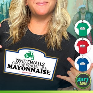 May include: A black t-shirt with a white and gold graphic that says "Whitewalls on the wheels like Mayonnaise - Downtown". The graphic also features a green scooter. The t-shirt is being modeled by a person. There are three other t-shirts in the image, one green, one red, and one blue, all with the same graphic.