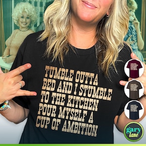Może przedstawiać: Czarny T-shirt z złotym tekstem, kt&oacute;ry brzmi "Tumble outta bed and I stumble to the kitchen pour myself a cup of ambition". Tekst jest w czcionce przypominającej pismo odręczne. Koszulkę nosi osoba.