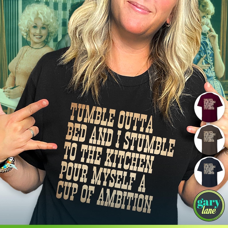 Może przedstawiać: Czarny T-shirt z złotym tekstem, kt&oacute;ry brzmi "Tumble outta bed and I stumble to the kitchen pour myself a cup of ambition". Tekst jest w czcionce przypominającej pismo odręczne. Koszulkę nosi osoba.