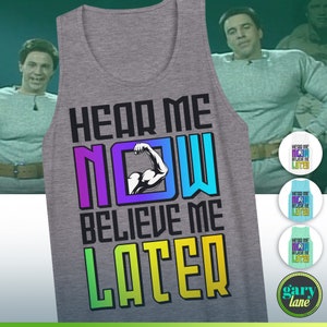 May include: A gray tank top with the text "Hear Me Now Believe Me Later" in rainbow colors. The text is in a bold, blocky font. A bicep with a muscle is in the middle of the word "NOW".