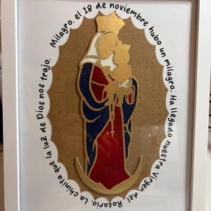 Puede incluir: Obra de arte religiosa enmarcada que representa a la Virgen María y el niño en oro, con detalles rojos y azules, sobre un fondo marrón. La imagen está encerrada en un marco blanco. Texto en español rodea la imagen central.