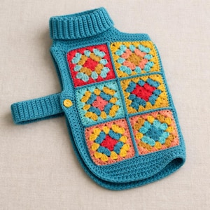 May include: A teal crochet dog sweater with a turtleneck and a strap with a button closure. The sweater features colorful granny squares in red, yellow, pink, and teal. The sweater is designed to fit a small dog.