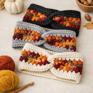 May include: Three crocheted headbands featuring a twisted front design. Each headband has a solid base color of black, gray, or cream, accented with a central band of multicolored yarn in shades of orange, yellow, brown, and deep red.