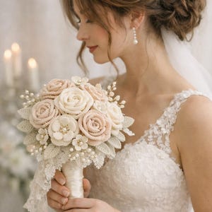 Può includere: Un bouquet di fiori all'uncinetto fatto a mano con rose color crema e rosa tenue, piccoli fiori bianchi e foglie verdi, impreziosito da perle bianche e finiture in pizzo. L'impugnatura è avvolta in un nastro di raso bianco con bordo in pizzo.