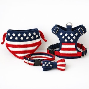 May include: A set of pet accessories featuring a crochet bandana, a harness, and a collar with a bow tie. Each item displays a red, white, and blue pattern with white stars on a navy blue background and horizontal stripes, including metal hardware.