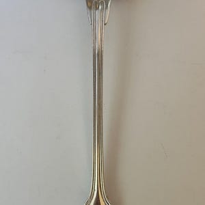 May include: A silver ladle with a rounded bowl and a long, slender handle. The handle has a decorative design with a heart-shaped end.