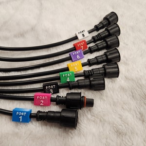 Peut inclure: Huit connecteurs électriques noirs avec des étiquettes numérotées de 1 à 8 et codées par couleur. Les étiquettes sont fixées aux connecteurs avec du texte blanc.