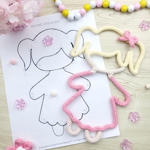 May include: A color-by-number illustration of a girl with a pink and cream-colored crocheted outline. The image includes the text "HOME IDEALIST" and copyright information. Decorative elements include pink flowers and wooden beads.